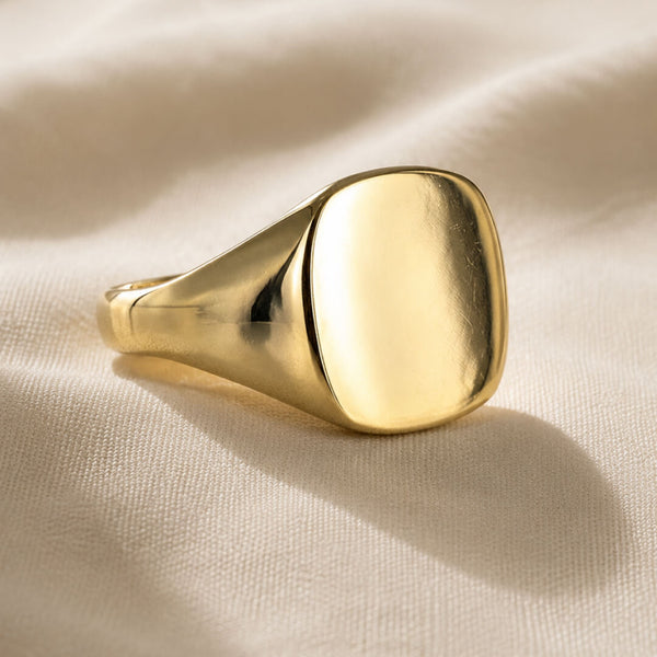 Star Jewellers Cushion Shape Signet Ring with a plain polished gold face on cream fabric